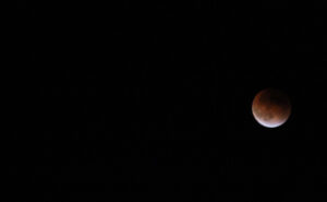 Image description: Photo of a black night sky with part of a pinkish colored moon peaking out.